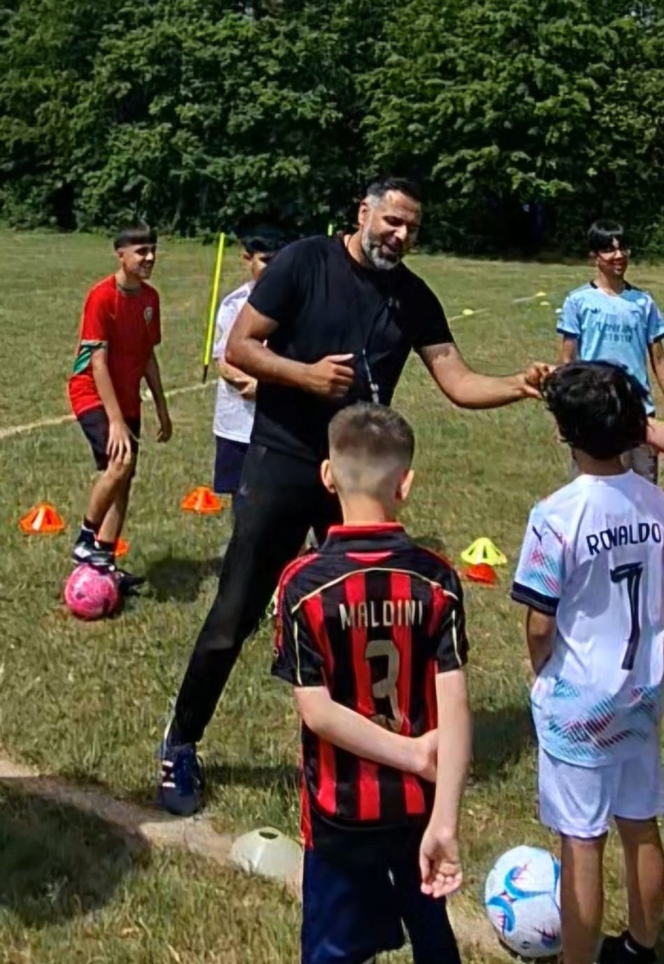Coach Imran high-fiving a young player during an Active Goals Football coaching session, with the group gathered round